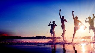 Four people in the shallow water happily jump into the air